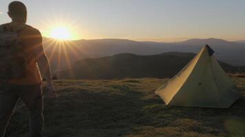 uma homem com uma mochila viaja dentro a montanhas. acampamento às pôr do sol. acampamento vida, fuga a partir de cidade. conceito do aventura, viagem. lento movimento cenas 4k video