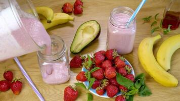 Strawberry Banana Smoothie is poured into a glass on the background of fresh fruits. Milkshake is ready to drink. The concept of healthy and vegetarian food. View from above video