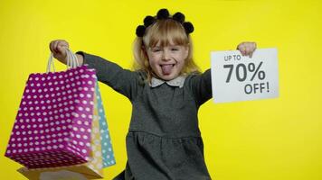 Child girl showing Up To 70 percent Off inscription sign and shopping bags. Teen pupil smiling video