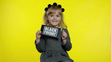 kind meisje tonen zwart vrijdag inscriptie, lachend, op zoek tevreden met laag prijzen, kortingen video