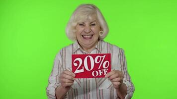 Senior grandmother showing 20 percent Off inscription sign, rejoicing good discounts, low prices video