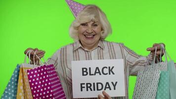 Inscription advertising Black Friday appears next to joyful grandmother with shopping bags video