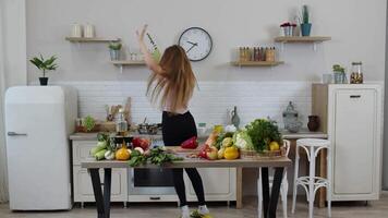 Lovely vegan girl with long hair dancing and singing in modern kitchen. Raw vegetable food diet video