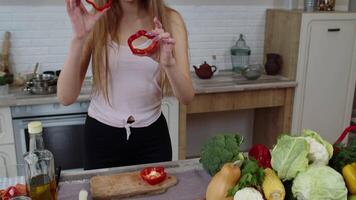 Joyful young girl vegan dancing holding fresh red slice of bell pepper on eyes. Healthy nutrition video