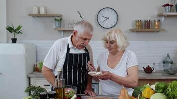 Senior couple in kitchen. Grandmother feeding grandfather with raw sprouts buckwheat with nuts video