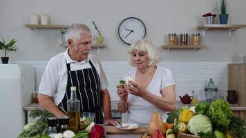 mayor Pareja en cocina. mayor abuela y abuelo comiendo crudo brócoli y coliflor video