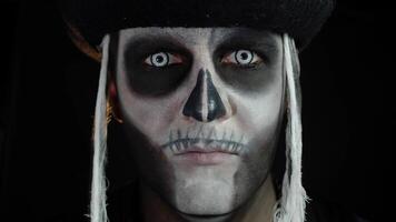 Scary man with carnival makeup of Halloween skeleton opening his eyes against black background video