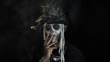 Sinister man with horrible Halloween skeleton makeup smoking cigar, making faces, looking at camera video