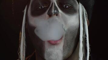 Portrait of scary guy in thematic costume of Halloween skeleton exhaling cigarette smoke from mouth video