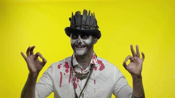 unheimlich Mann mit schrecklich Halloween Skelett Make-up machen Gesichter, suchen beim Kamera, zeigen in Ordnung Zeichen video