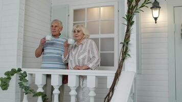 Senior elderly Caucasian couple drinking coffee, looking ahead in porch at home. Mature family video