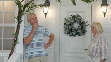 Senior couple together in porch at home. Mature man stands and his wife comes to embrace him video