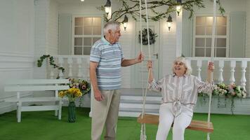 Senior couple together in front yard at home. Man swinging woman. Happy elderly pensioners family video