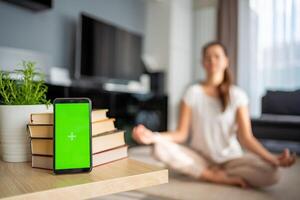 Digital detox concept. Smartphone with green chroma key screen and woman meditating in background photo