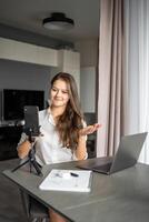 A young woman blogger conducts an educational broadcast on a laptop in social network in home workplace, online teaching concept photo