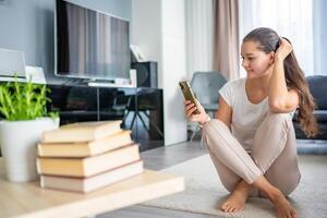 un joven mujer es molesto a leer un libro pero es constantemente distraído por su teléfono inteligente y social redes foto