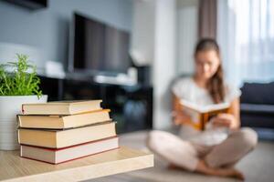 Stack of books in the foreground and woman reading book in the background photo