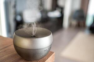 Grey aroma oil diffuser on light table at home, space for text. Air freshener photo