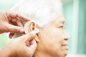 Doctor install hearing aid on senior patient ear to reduce hearing loss problem. photo