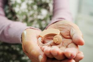 Asian senior woman patient using hearing aid in ear to reduce hearing loss problem. photo