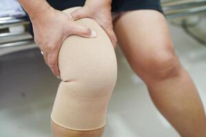 Asian senior woman wearing elastic support knee brace for reduce pain. photo