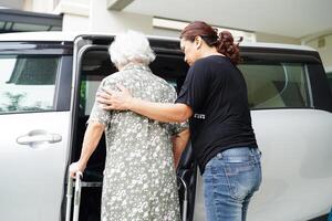 cuidador ayuda a una anciana asiática con discapacidad a entrar en su automóvil, concepto médico. foto