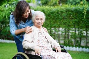 cuidador ayuda a una anciana asiática con discapacidad a una paciente sentada en silla de ruedas en el parque, concepto médico. foto