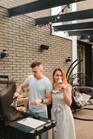 un casado Pareja cocineros A la parrilla carne juntos en su terraza foto