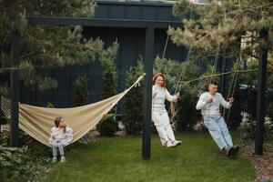 Mom and dad are riding on a swing, and their daughter is on a hammock next to them. The family is resting on a swing photo