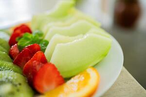 mixed fruit plate containing melon, strawberries, oranges and kiwi. The main focus is on melons. photo