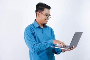 sonriente o contento asiático empresario con lentes participación ordenador portátil vistiendo azul camisa aislado en blanco antecedentes foto