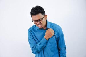 asiático joven hombre con lentes participación su cofre en cofre dolor o coronario corazón enfermedad vistiendo azul camisa aislado en blanco antecedentes foto