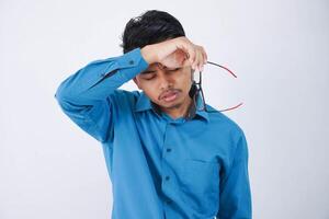 retrato de agotado hermoso joven asiático empresario en vistiendo azul camisa tomando apagado lentes siente cansado después trabajando en computadora aislado en blanco antecedentes foto