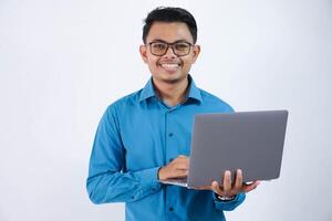 sonriente o contento asiático empresario con lentes participación ordenador portátil vistiendo azul camisa aislado en blanco antecedentes foto