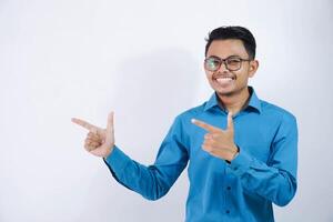 Handsome asian male employee with glasses smiling in a pose finger pointing to the side wearing blue shirt isolated on white background photo