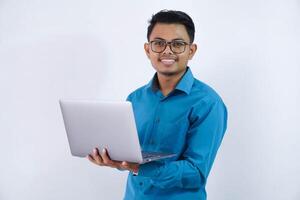 smiling or happy asian businessman with glasses holding laptop wearing blue shirt isolated on white background photo