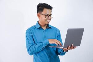 sonriente o contento asiático empresario con lentes participación ordenador portátil vistiendo azul camisa aislado en blanco antecedentes foto