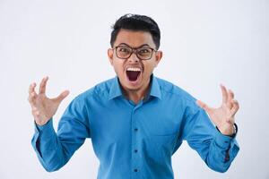 irritado hermoso joven asiático hombre con lentes en vistiendo azul camisa levanta palmas mientras gritos ruidosamente aislado en blanco antecedentes foto