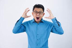 irritado hermoso joven asiático hombre con lentes en vistiendo azul camisa levanta palmas mientras gritos ruidosamente aislado en blanco antecedentes foto