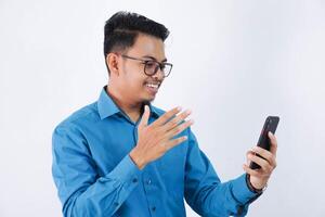 empleado asiático hombre sonriente participación teléfono en un vídeo llamada con un cliente vistiendo azul camisa aislado en blanco antecedentes foto