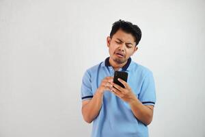 triste cara con participación teléfono joven asiático hombre vistiendo azul polo t camisa aislado en blanco antecedentes. irritado cara expresiones foto