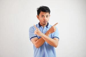 retrato de un pensativo joven asiático hombre brazos cruzado con dedos señalando arriba vistiendo azul t camisa aislado en blanco antecedentes foto