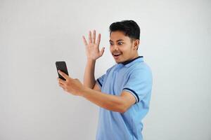 emocionado o contento joven asiático hombre participación teléfono y abrió su palmas vistiendo azul polo t camisa aislado en blanco antecedentes foto