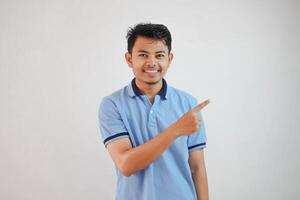 sonriente asiático hombre con dedos señalando a el lado vistiendo azul t camisa aislado en blanco antecedentes foto
