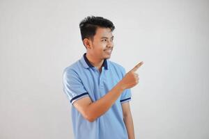 sonriente asiático hombre con dedos señalando a el lado vistiendo azul t camisa aislado en blanco antecedentes foto