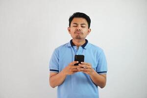 triste cara con participación teléfono joven asiático hombre vistiendo azul polo t camisa aislado en blanco antecedentes. irritado cara expresiones foto