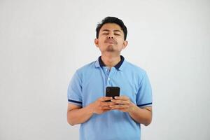 triste cara con participación teléfono joven asiático hombre vistiendo azul polo t camisa aislado en blanco antecedentes. irritado cara expresiones foto