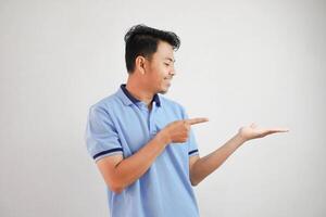 smiling asian man with an open hand with fingers pointing to the side wearing blue t shirt isolated on white background photo