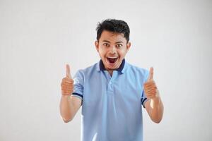 Portrait of cheerful asian man in wearing blue t shirt smiling and showing thumbs up at camera isolated over white background photo