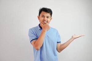 serious face asian man with an open hand the side and while holding the chin wearing blue t shirt isolated on white background photo